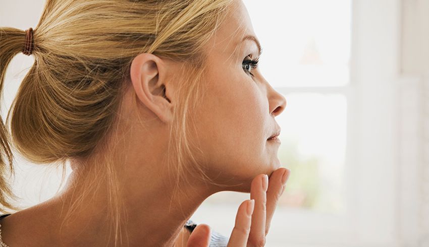 the side profile of a woman examining her face in a mirror